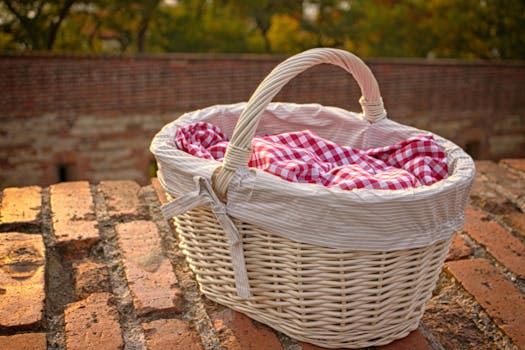 A charming wicker picnic basket with checkered fabric, set against a rustic brick wall outdoors.